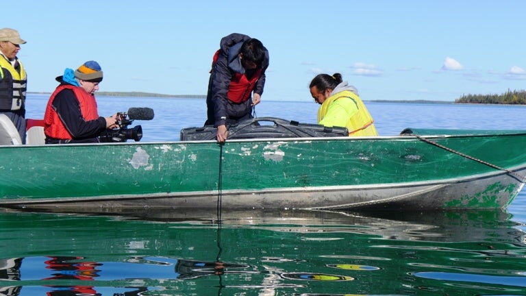 Alan filming youth using an Eckman Sampler to take a sediment sample